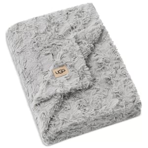 A soft, grey faux fur blanket with the UGG logo on a tan patch, featuring a textured, plush design.
