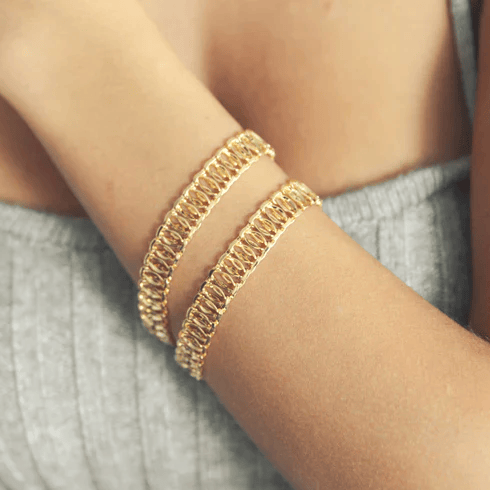 Two gold chain bracelets are shown on a person's arm, worn with a gray sleeveless top.