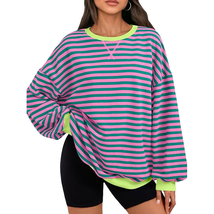 A woman is wearing an oversized long-sleeve shirt with green and pink horizontal stripes. The shirt has neon green cuffs and collar, paired with black shorts.
