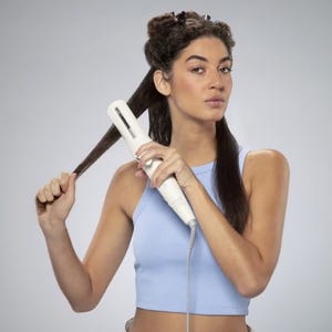 A woman is using a flat iron to straighten her hair.