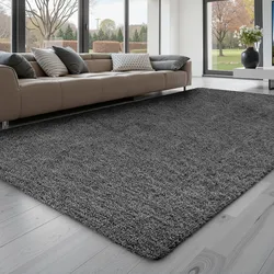 A cozy gray shag rug lies on a light wooden floor in front of a modern beige sectional sofa with various gray pillows, set in a spacious living room with large windows.