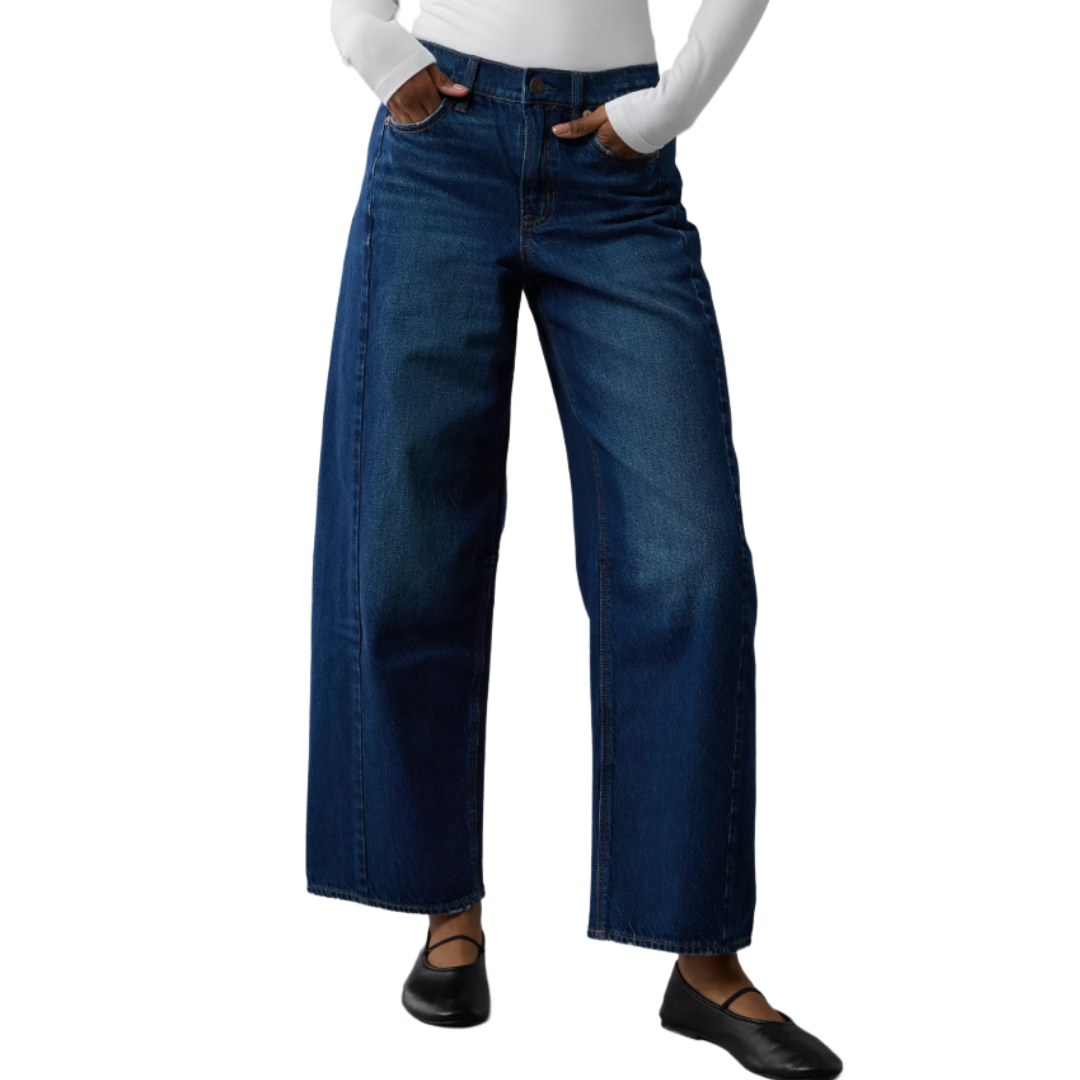 Wide-leg blue jeans paired with a white long-sleeve top and black flat shoes.