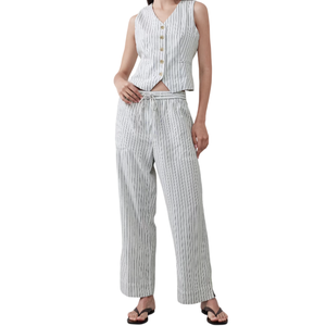 A woman is wearing a sleeveless, buttoned vest and drawstring pants with a grey and white striped pattern, paired with black flip-flops.