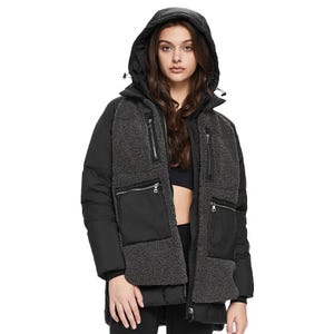 A woman is wearing a hooded black puffer jacket with zippered pockets and gray textured accents, paired with a black top and pants.