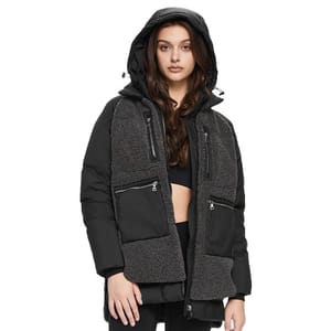 A woman is wearing a hooded black puffer jacket with zippered pockets and gray textured accents, paired with a black top and pants.