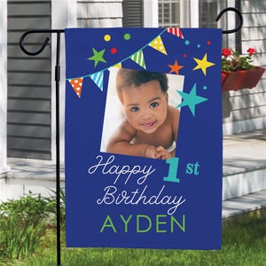 Blue garden flag featuring a photo of a baby with colorful stars, bunting, and text reading \“Happy 1st Birthday Ayden.\“