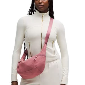 A person wears a pink crossbody bag paired with a white zippered jacket and matching pants.