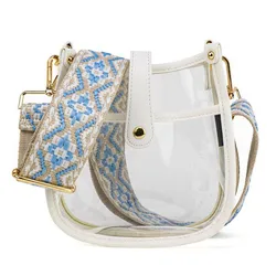 A clear handbag with white accents and a wide, adjustable shoulder strap featuring a blue and beige geometric pattern, adorned with gold-tone hardware.