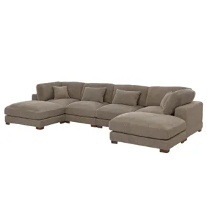 Large L-shaped sectional sofa in brown corduroy with multiple cushions, placed on a light-colored textured rug in a spacious, well-lit living room with large windows, a chandelier, and a bookshelf.