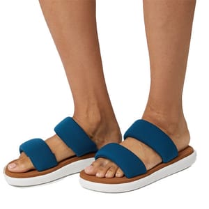 A pair of blue slide sandals with two wide straps and white soles are worn on a person's feet.