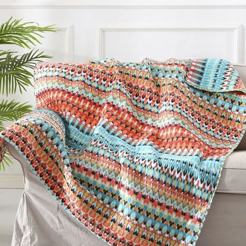 A colorful crocheted blanket with zig-zag patterns draped over a couch.