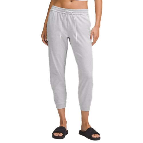 A person wears light gray jogger pants with an elastic drawstring waist and black slide sandals.