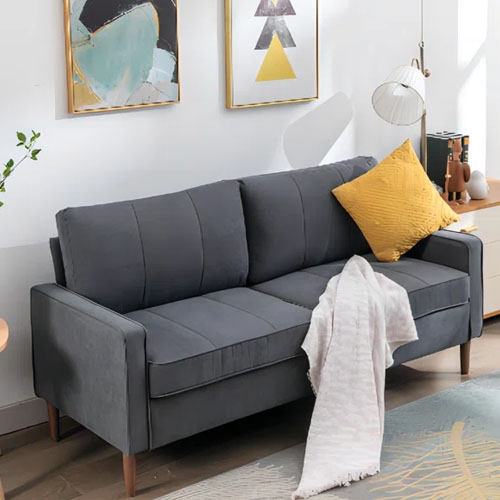 A gray sofa with a yellow cushion and a white throw blanket, set against art-adorned walls.