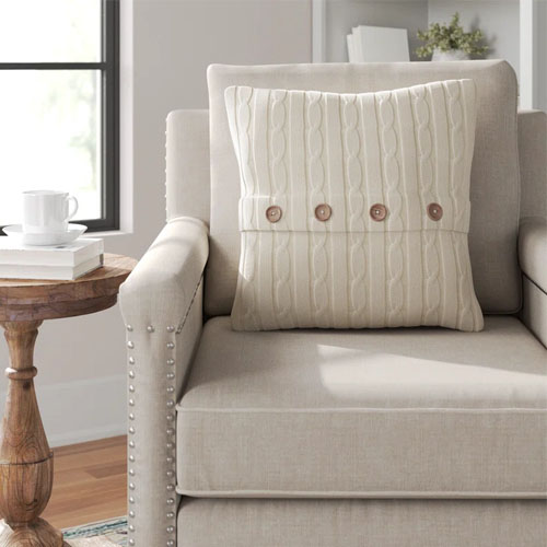 a cream colored pillow with four brown buttons on a tan colored armchair