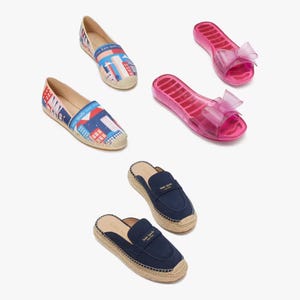 Three pairs of women's shoes: two slip-on espadrilles, one with a cityscape print, one navy blue, and one pair of pink jelly sandals with a bow.