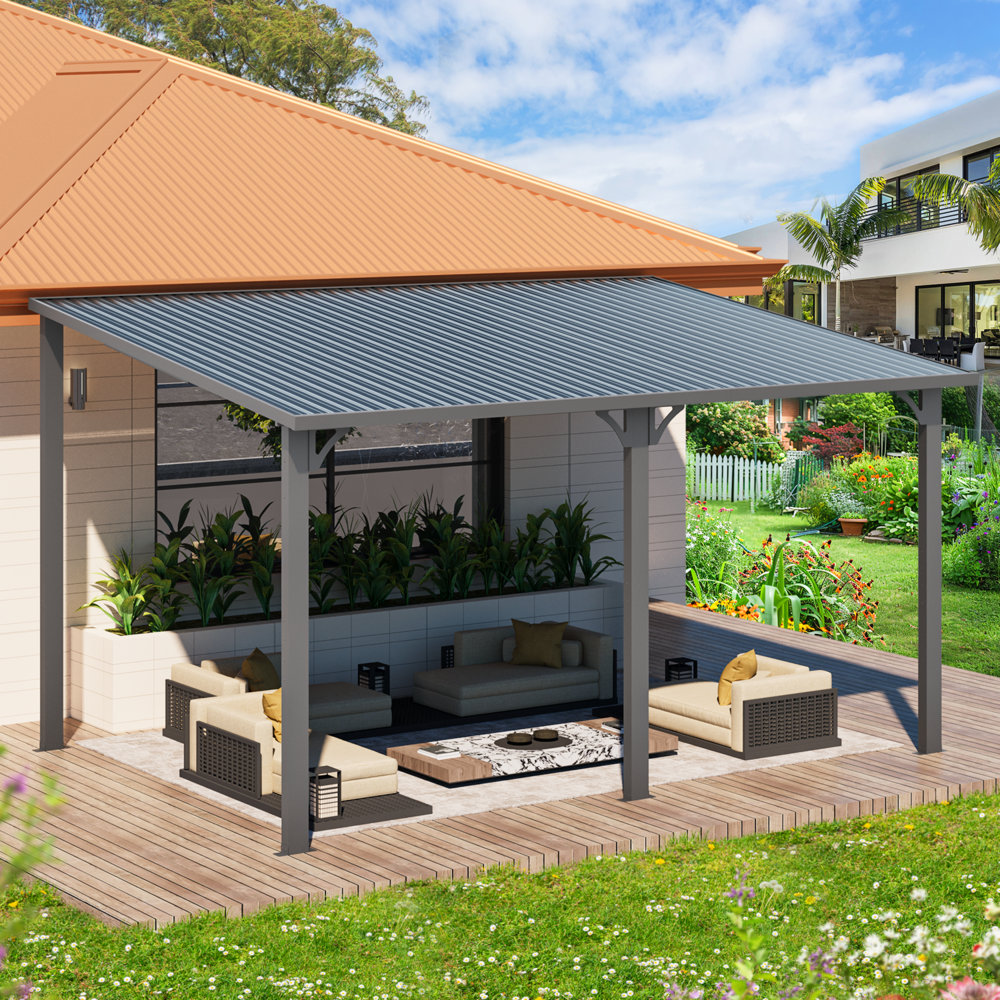 A modern outdoor patio features a metal-roofed pergola over wooden decking with cushioned seating, a low coffee table, and surrounding greenery.