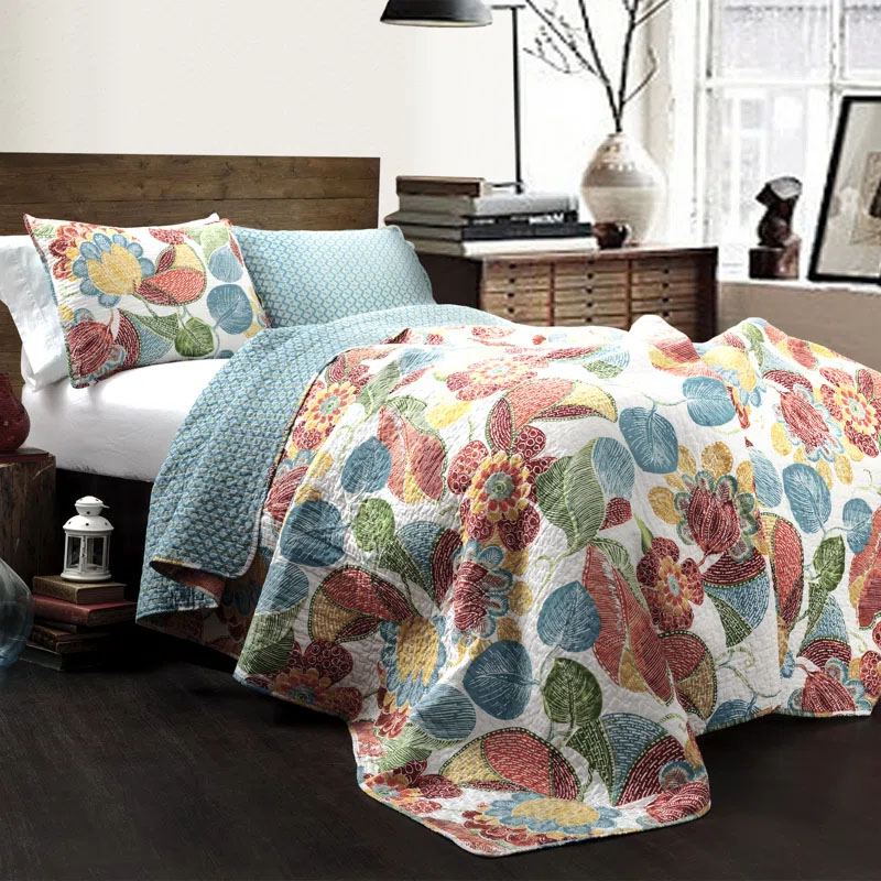 A colorful King Reversible Quilt Set with a vibrant floral pattern featuring red, yellow, blue, and green leaves and flowers on one side and a blue geometric pattern on the reverse, accompanied by matching pillowcases.