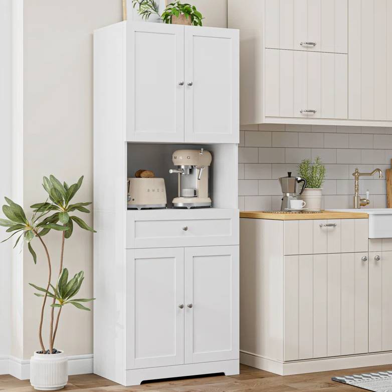 A tall white kitchen pantry with upper and lower cabinets, a small drawer in the middle, features an open shelf holding a cream-colored espresso machine and toaster, complemented by a potted plant on top.