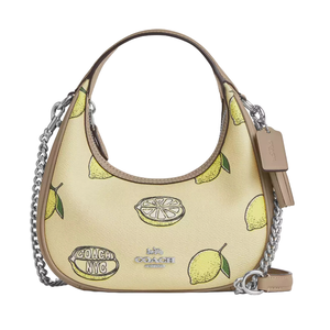 Coach Carmen Bag features a lemon print on a light background with silver chain detailing and a leather strap. It's accented by a \“Coach NYC\“ logo, adding a playful touch to the design.