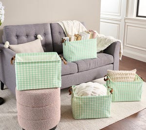 4-piece collapsible storage basket set with light green and white gingham pattern, featuring brown leather-like handles, used for organizing items like books, pillows, and blankets on and around a gray sofa.