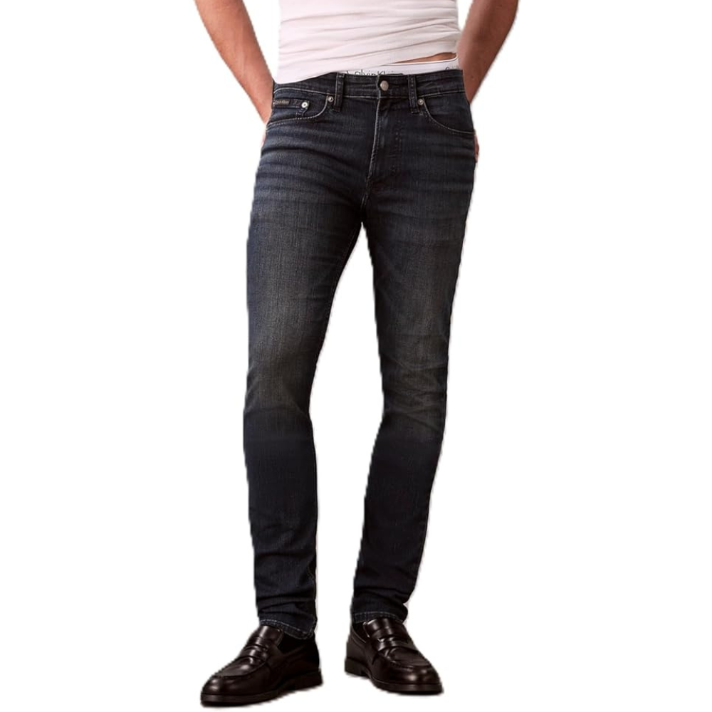 A person is wearing dark blue slim-fit jeans paired with black loafers, with a white shirt tucked in at the waist.