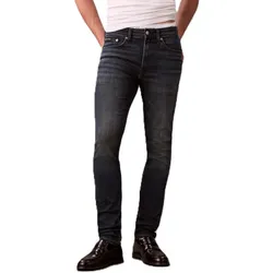 A person is wearing dark blue slim-fit jeans paired with black loafers, with a white shirt tucked in at the waist.
