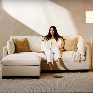 A neutral-colored PillowTop Sectional with soft, textured fabric, featuring a chaise lounge and large woven cushions. It includes hidden storage for practical use in living spaces.