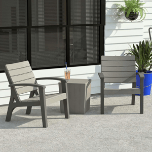 Two outdoor chairs with a matching side table between them, all made of dark and light grey plastic, accompanied by potted plants.