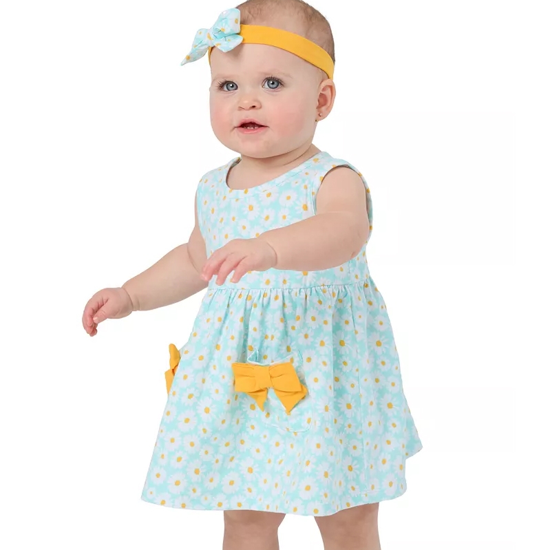 A baby wearing a sleeveless light blue dress with a daisy pattern and yellow bows, paired with a matching headband.