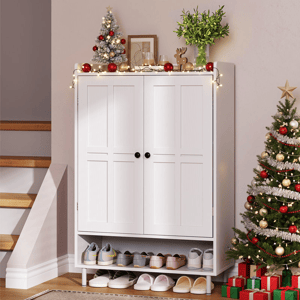 A white cabinet with shoe storage underneath is adorned with holiday decorations, including small Christmas trees, string lights, and festive ornaments. Nearby, a larger Christmas tree stands beside a stack of wrapped gifts.