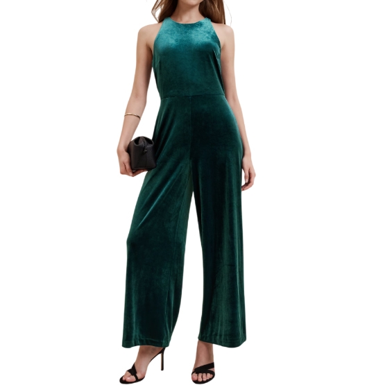 A green velvet jumpsuit with a sleeveless, halter neckline, featuring a fitted top and wide-leg pants. Paired with black high heels and a small black clutch.