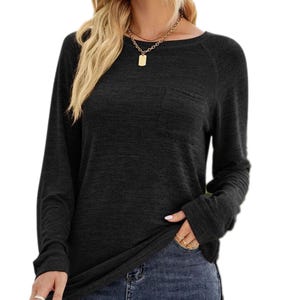 A black long-sleeve top with a round neckline and chest pocket, paired with jeans. It features a casual fit and is accessorized with a gold chain necklace and rings.