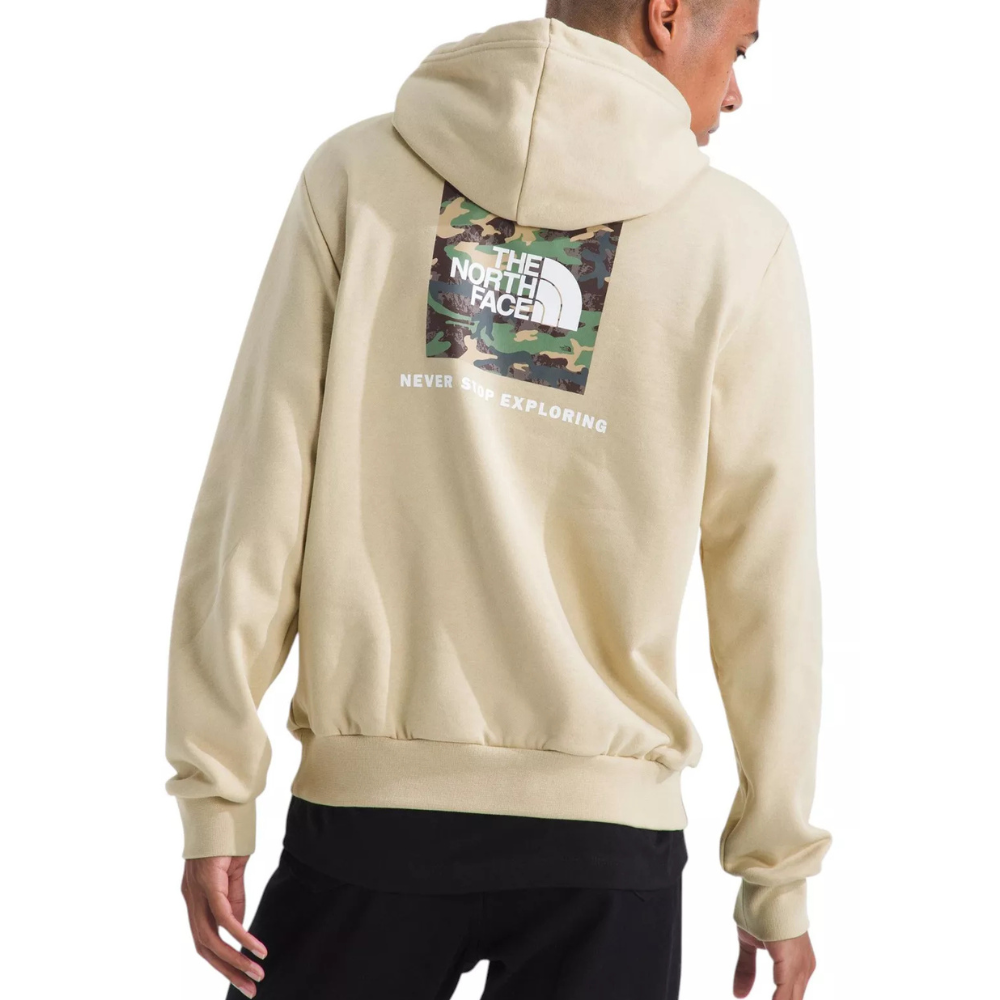 Tan hoodie with a camo-patterned North Face logo and \“Never Stop Exploring\“ text on the back, paired with black pants.