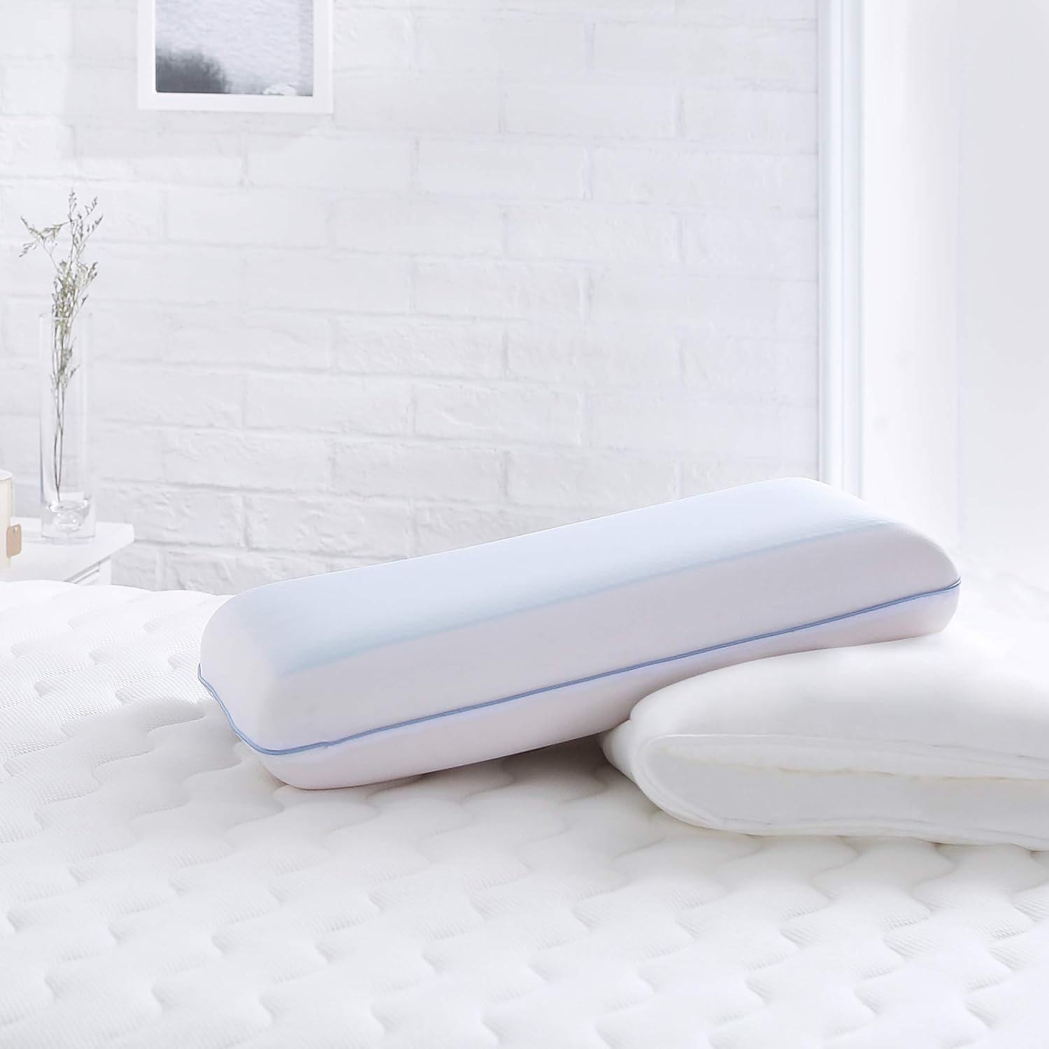 Memory foam pillow with a blue piping edge on a mattress in a white brick-walled room.