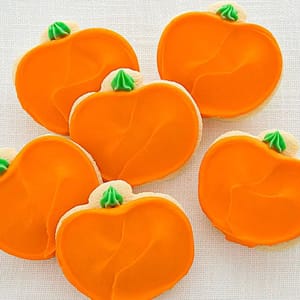 Sugar cookies decorated to look like orange pumpkins with green stems.