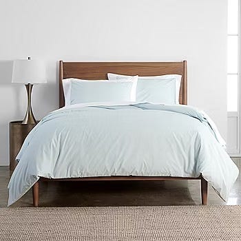 3-piece queen duvet set in light blue includes a duvet cover and two matching pillow shams, styled on a wooden bed with a white lamp beside it, placed on a woven rug.