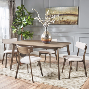 A modern dining set featuring a wooden table with four chairs, all with light upholstery. The setting includes a large decorative vase with white flowers, a green plant, and a textured area rug.