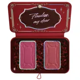 A red makeup palette opens to reveal two rectangular blush pans, encased in a decorative package with the phrase \“Flawless, my dear\“ on the inner lid.