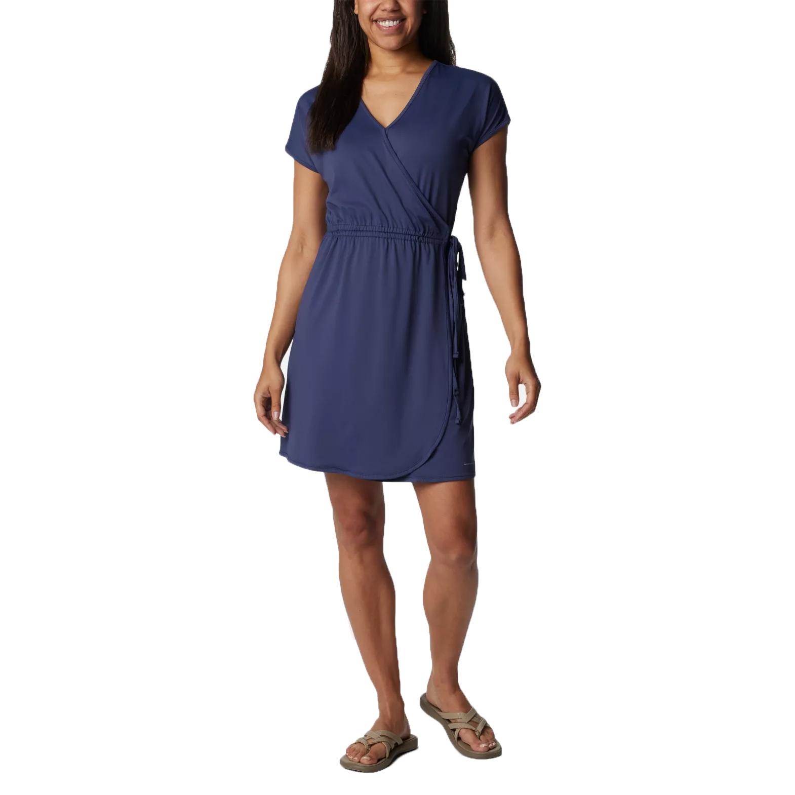 A woman is wearing a short-sleeve, blue wrap dress with a V-neck and tie at the waist, paired with casual sandals.