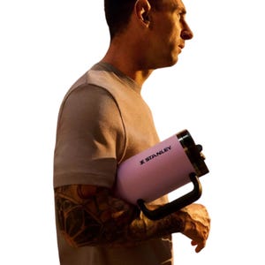 A person is holding a large Stanley mug, featuring a handle and a lid, against a white background.