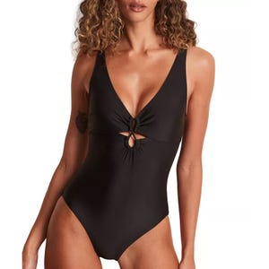 Black one-piece swimsuit with a deep V-neckline, front cut-out details, and wide shoulder straps. Features a ruched design and is made to smooth the body's silhouette.