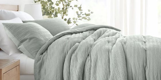 a bed with white sheets and a green blanket and green pillows