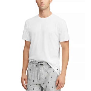 A man models a white, short-sleeve Polo Ralph Lauren cotton sleep shirt paired with drawstring gray pajama pants featuring a small polo player pattern.
