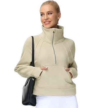A woman is wearing a beige high-neck pullover with a front zipper, paired with white leggings and white sneakers. She carries a black shoulder bag.
