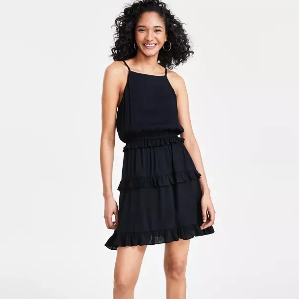 A woman wearing a black tiered ruffle dress with a sleeveless design and hoop earrings.