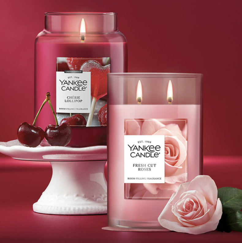 Two Yankee Candle fragrances: \“Chérie Lollipop\“ with cherries and \“Fresh Cut Roses\“ featuring a rose, displayed on a red background.