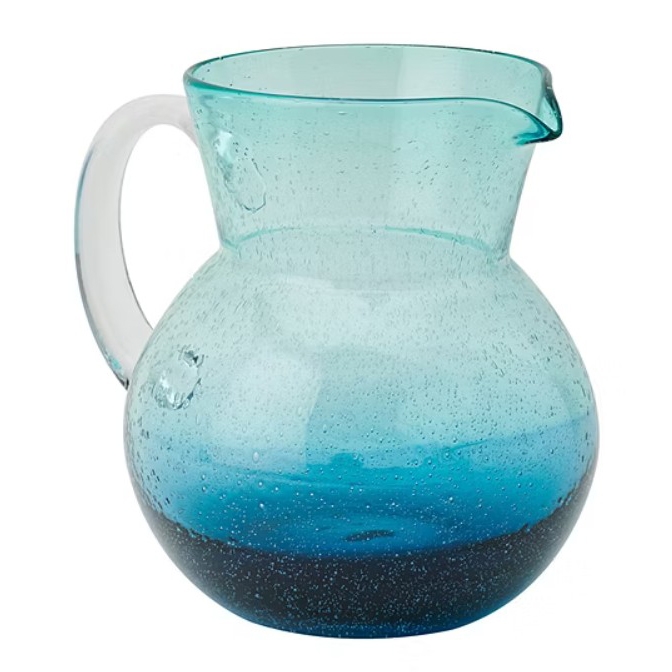 A translucent glass pitcher with an ombre effect, transitioning from light blue at the top to a darker blue at the bottom. It features a wide body, a curved handle, and a spout for pouring.