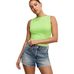 A woman is wearing a bright green sleeveless top and denim shorts.