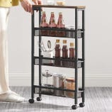 A compact rolling storage cart featuring three-tiered mesh shelves, containing bottles, spices, utensils in a container, and jars, ideal for kitchen organization. It has a metal frame, a wooden top, and four wheels for easy mobility.
