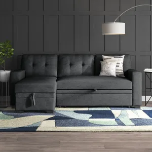Dark gray sectional sofa with tufted cushioning, accompanied by a geometric rug and a floor lamp with a round shade. Nearby is a small side table with books and a potted plant.